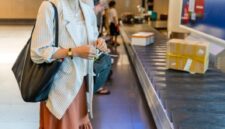 Seorang wisatawan menyiapkan paspor dan tiket penerbangan di bandara internasional sambil memegang dokumen asuransi perjalanan yang memberikan perlindungan selama berada di luar negeri.